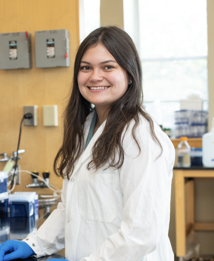 Picture of Savannah smiling in a lab coat working in the lab.